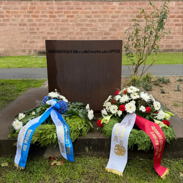 Am heutigen Tag jährt sich die Verkündung der „Nürnberger Rassengesetze“ zum 90. Mal. Die „Nürnberger Rassengesetze“ wurden am 15. September 1935
während des 7. Reichsparteitags der NSDAP vom dazu eigens einberufenen und im damaligen Nürnberger Kulturvereinshaus am Frauentorgraben tagenden Reichstag erlassen. Das „Blutschutzgesetz“ verbot Eheschliessungen zwischen Juden und „Deutschblütigen“; das „Reichsbürgergesetz“ würdigte alle Menschen jüdischen Glaubens zu Staatsbürgern mit eingeschränkten Rechten
herab. Auf direkte Anweisung von Reichsinnenminister Frick vom 3. Januar 1936 wurden Sinti und Roma ebenso den diskriminierenden Bestimmungen der „Nürnberger Gesetze“ unterworfen. Verbindungen zwischen Sinti/Roma und Nicht-Sinti/Roma wurden untersagt und unter Strafe gestellt. Zahlreiche Angehörige der Minderheit wurden in der Folgezeit wegen sogenannter „Rassenschande“ in Konzentrationslager deportiert. Auf Einladung des Landesverbands der Sinti und Roma und ihres Vorsitzenden Erich Schneeberger haben wir deshalb mit dem Oberbürgermeister der Stadt Nürnberg an einer Kranzniederlegung zu Ehren der ermordeten Nürnberger Sinti und Roma gedacht. In Zeiten, in denen Antiziganismus und Antisemitismus wieder deutlich zunehmen, ist es wichtig zu zeigen dass beides bei uns, in der Stadt der Menschenrechte, keinen Platz hat.